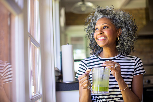 Black woman smiling while holding green smoothie