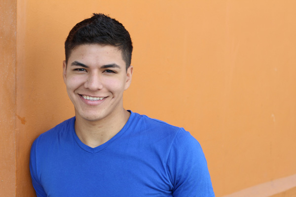 Young man smiling while leaning against a wall