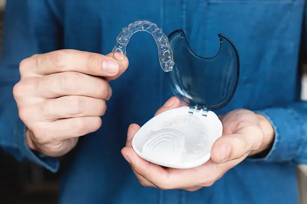 Hands holding a clear aligner and its storage case, emphasizing care and convenience for adult orthodontic treatment.