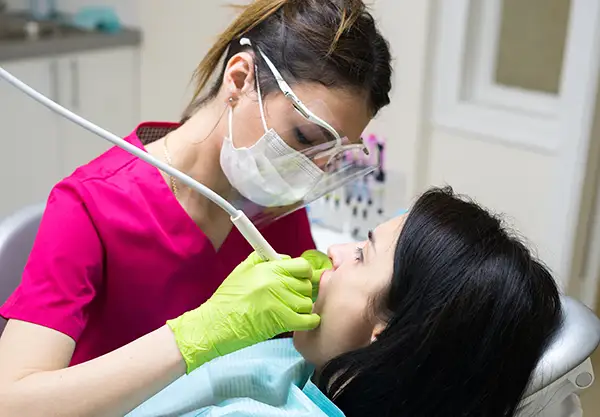 A dental hygienist completing a routine dental cleaning procedure on the teeth of a relaxed female patient.