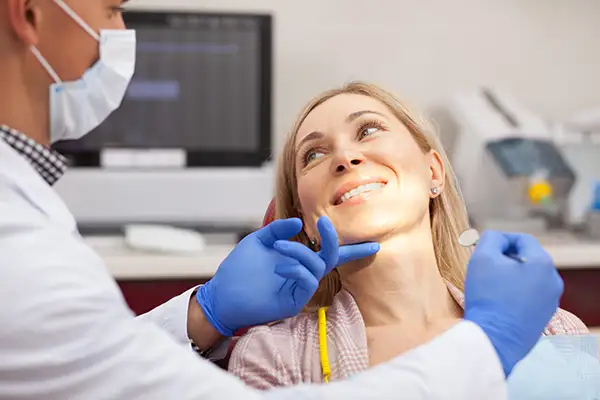Dentist performing a dental check up on a smiling patient, highlighting the importance of regular preventive dental care. 