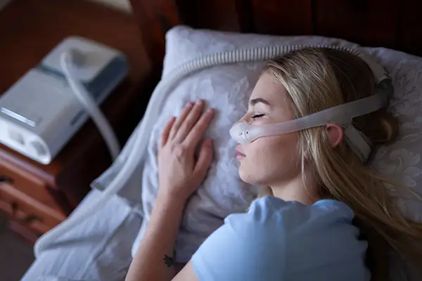 Woman sleeping with a CPAP mask connected to a machine, effectively managing sleep apnea. 